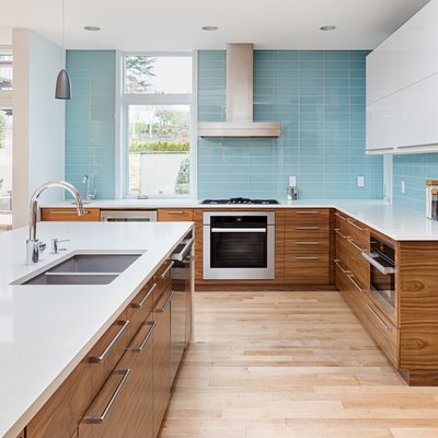 beautiful modern kitchen in new contemporary style luxury home, with island, pendant lights, hardwood floors, and stainless steel appliances. Features blue tone tile that extends to the ceiling