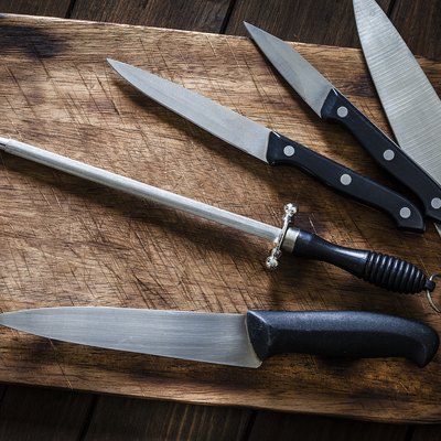 Sharpening steel and various kitchen knives on wooden cutting board