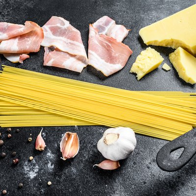 Ingredients for traditional italian pasta alla carbonara. Uncooked spaghetti, pancetta bacon, parmesan cheese, egg. Black background. Top view