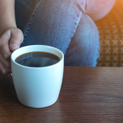 Closeup image of a woman's hand holding a cup of hot coffee to drink while sitting in cafe