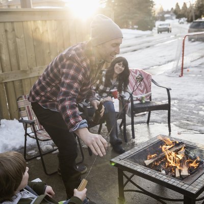 Family roasting marshmallows at fire pit in snowy driveway