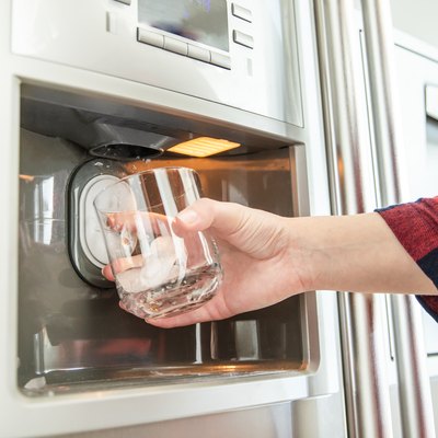 Woman's hand holds glass and uses refrigerator to make fresh clean ice cubes.