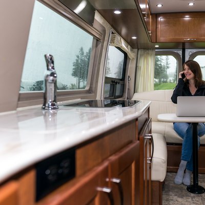 Young Woman Talking on phone and Using Laptop Inside Motorhome