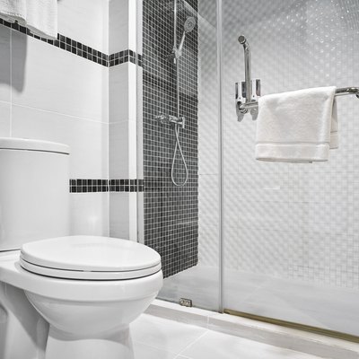 Shower and toilet in modern white bathroom with black tile accents.