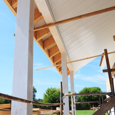 Building house patio roofing with wooden pillars and unfinished soffits and fascia boards installation.