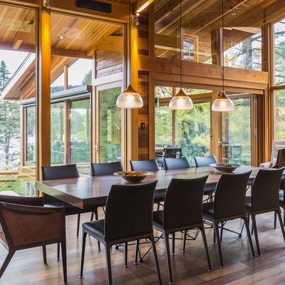 Wooden dining table with rawhide armchairs, black leather chairs and illuminated industrial style copper with  frosted glass pendant lighting fixtures in dining area of great room with Ipe wood floor inside luxurious stained cedar and timber wood home wi