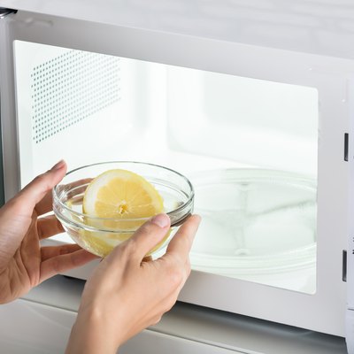 Woman Putting Bowl Of Slice Lemon In Microwave Oven