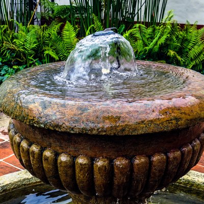 Top of antique water fountain with garden in background