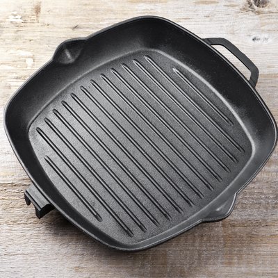 New empty cast aluminum grill pan with two handles on a wooden background.