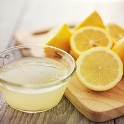 Small glass bowl of lemon juice and several lemon halves arranged on a wooden cutting board