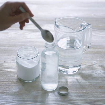 Adding powdered borax to bottle of water, using spoon, close-up