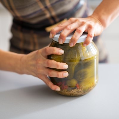 closeup on young housewife opening jar of pickled cucumbers