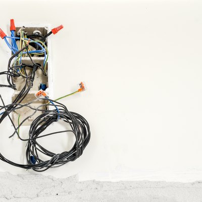 Circuit breakers and fuses in a plastic box on a wall with wires hanging out and unplugged