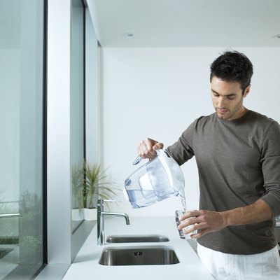 Man in kitchen pouring glass of filtered water