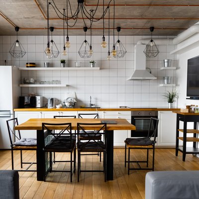 Modern scandinavian an eat-in kitchen interior design with big wooden table and chairs against light wood floor, bright white walls and furnitures with TV, appliances and hanging light bulbs