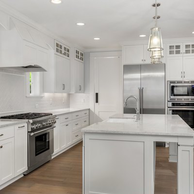beautiful white kitchen in new luxury home with island, pendant lights, and hardwood floors. Features stainless steel appliances and farmhouse style sink