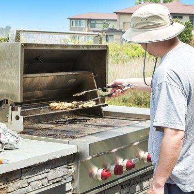 Man barbecuing chicken on a outdoor gas grill