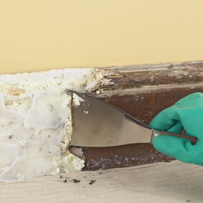Using a scraper to remove paint from skirting board covered with paste stripping solution