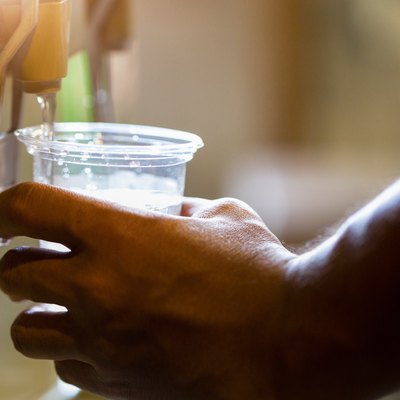 Male hand serving water of a water cooler in plastic cup.