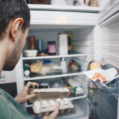 Man holding egg carton by refrigerator in kitchen