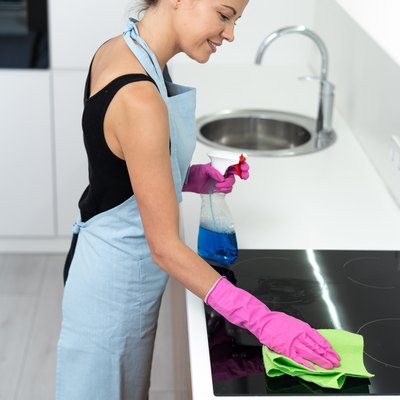 Young adult woman cleaning electric stove in kitchen