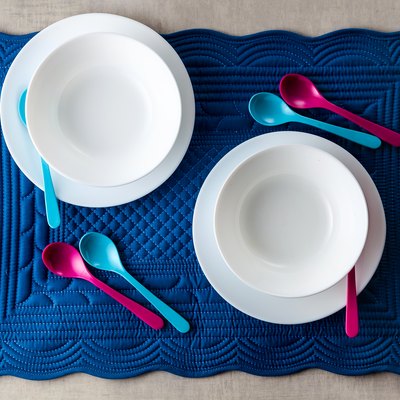 A set of baby dishes on a blue soft napkin for breakfast. kitchen table accessories for serving. Colored small spoons.