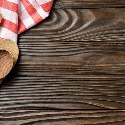 Red checkered napkin and wooden utencils on brown wooden kitchen table with copy-space. Top view