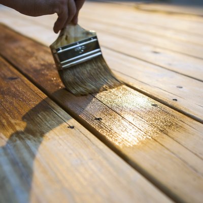 Male Carpenter Applying Varnish To Wooden Deck