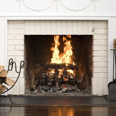 White brick fireplace with fire burning, stack of logs on rack, and fireplace tools