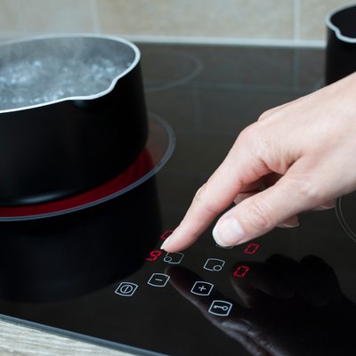 Close Up Of Woman Adjusting Temperature Of Halogen Hob In Kitchen