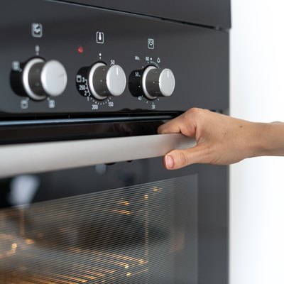 Woman holding handle modern built in oven and opening glass door