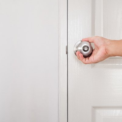 Hand of a person turning doorknob, white door and wall
