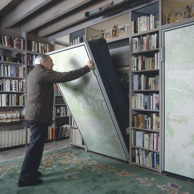 Senior man pulling Murphy bed in library of a traditional house