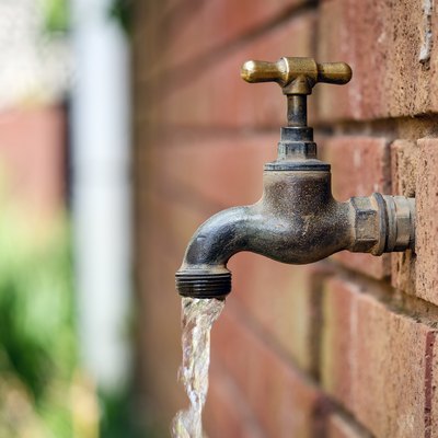 Close-Up Of Water Running From Faucet At Brick Wall