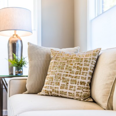 Closeup of two pillows on couch or sofa by bright window in modern apartment, house or home with staging of large beige, neutral white colors, lamp