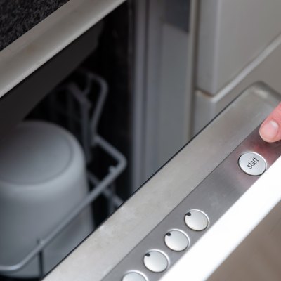 Close up of finger pressing start button on dishwasher in the kitchen. Hand starting dish washer machine