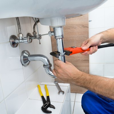 Male Plumber Fixing Sink In Bathroom