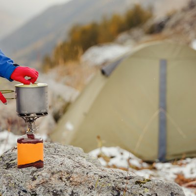 gas cartridge camping jet stove with modern titanium pot on it on a background of the tent during hiking