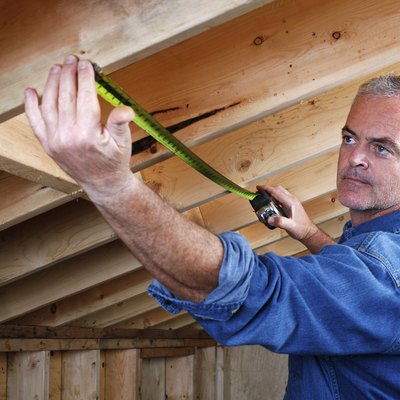 Man measuring distance between rafter beams of home addition.