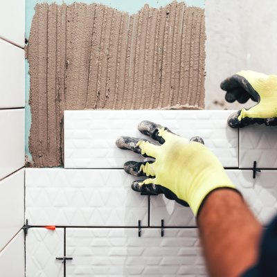 construction worker installing small ceramic tiles on bathroom walls and applying mortar with trowel