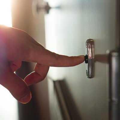 Finger pressing doorbell in sunny apartment building corridor. Close up of male hand ringing door bell in a block of flats. Salesman, fundraiser, guest or visitor behind door.