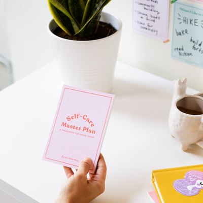 hand holding pink journal over white desk with plant