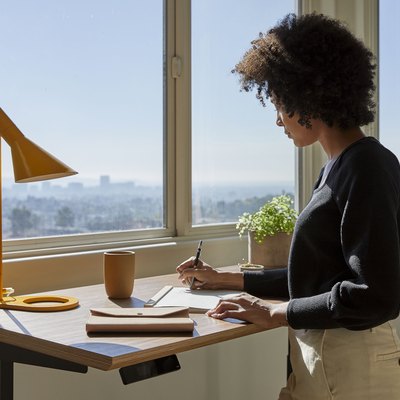 person at standing desk with lamp near window