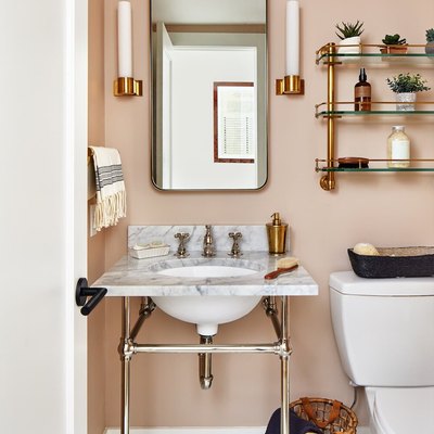 pink powder room with glass bathroom shelving above the toilet and next to a vanity mirror