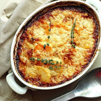 Grandbaby Cakes Potato and Squash Gratin in casserole dish with herbs on top