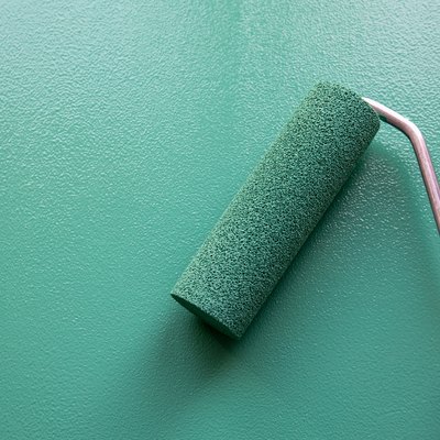 Paint roller with green or teal color on painted wooden surface.