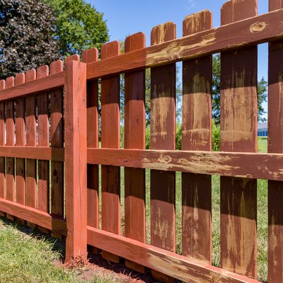 Wooden privacy fence in backyard with pickets being painted red