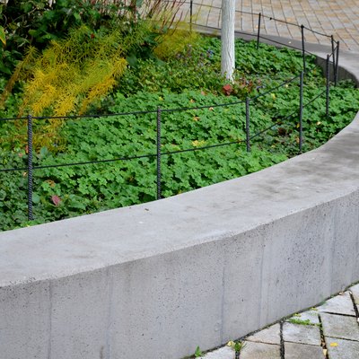autumn yellow coloration of perennial vegetation in an elevated flowerbed. the gray concrete wall serves as a bench. in some places it turns into an arch. granite paving of granite cubes. gardener collects garbage in a bag with pliers