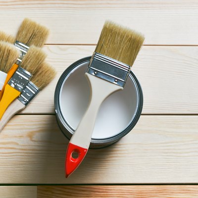 A Clean Brush On A Can Of White Paint. There Are A Lot Of Different Brushes Next To It, On A Wooden Background. Painting And Repair Work. The concept of the construction industry, professional and home repair.
