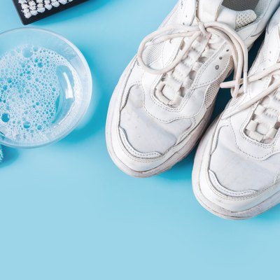 Dirty white sneakers with special tool for cleaning them on blue.